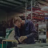 Young metal worker using power tool in factory with protective equipment